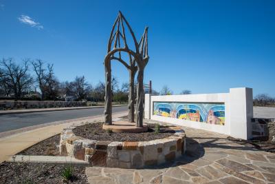 Pair of concrete sculptures using method called trabajo rustico to form three life-like cedar tree limbs which stand upright and form a series of interconnected arches. Sculptures are approximately 11 ft 5 in tall and 5 ft wide. The sculptures sit on a concrete base within a planter bed and seat wall.