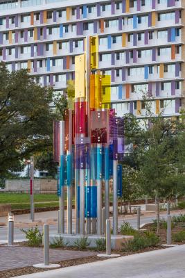 A grouping of stainless-steel poles with various colored architectural glass referencing the cultural and dynamic rhythm of San Antonio. A total of 9 stainless-steel, brush-finished poles and various colored architectural glass including blue, orange, pink, and yellow glass.